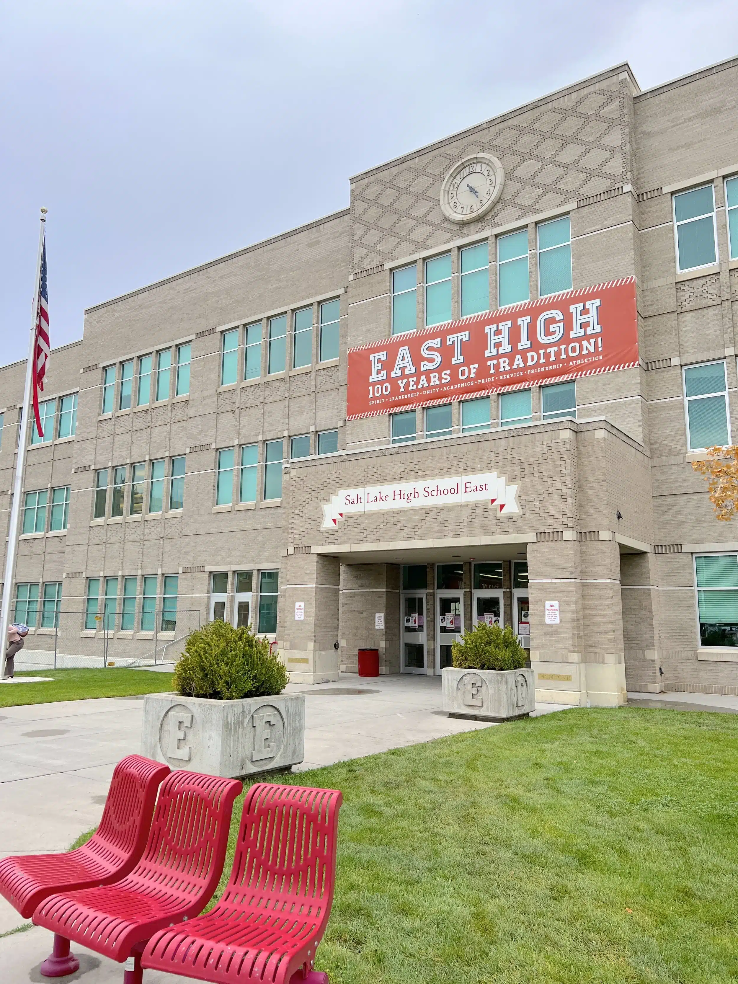 The iconic brick front exterior of East High School in Salt Lake City at an angle, showing the main entrance, red chairs, and the school name on the front facade.