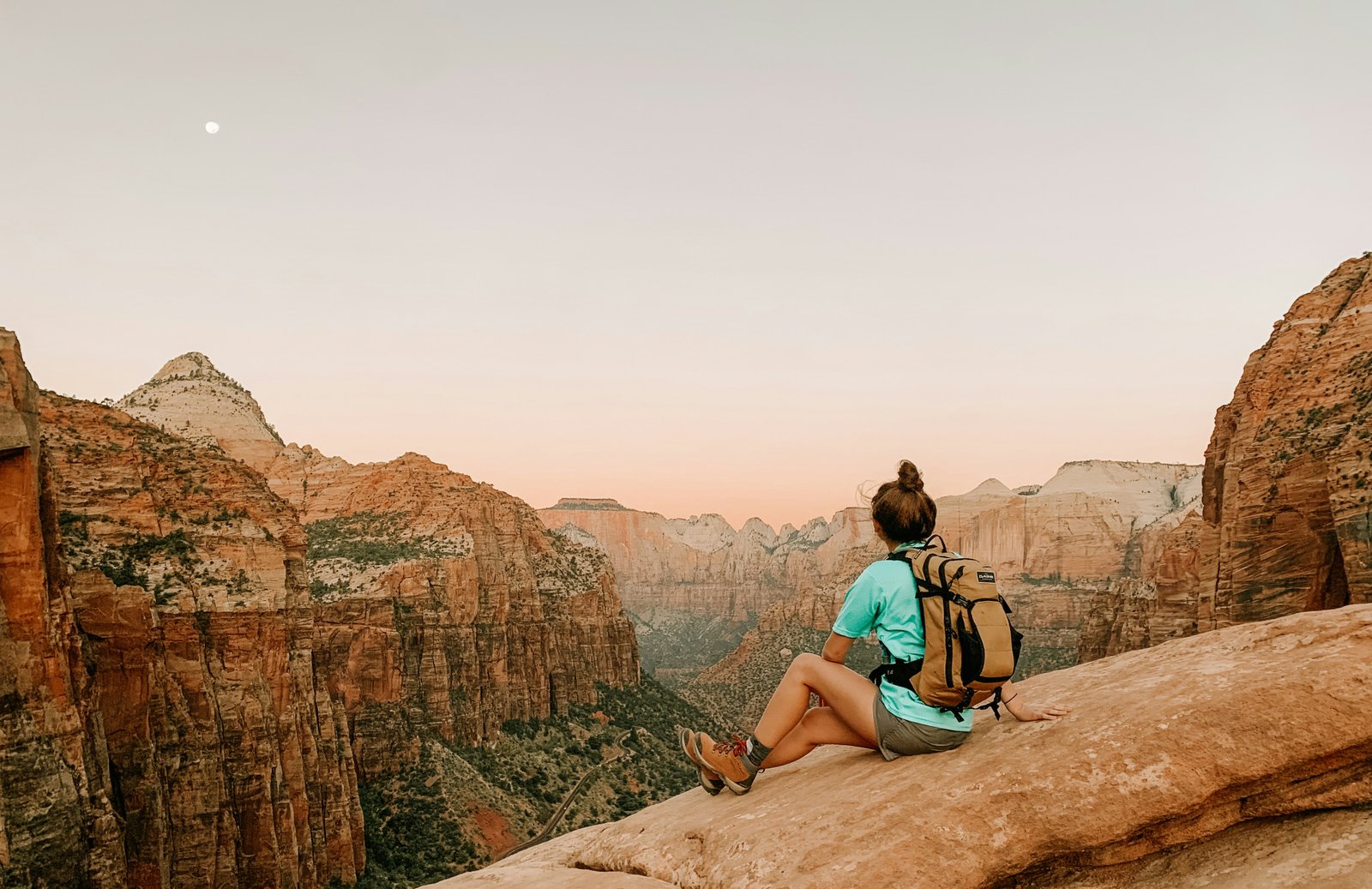 Hiker sitting on a high rock ledge overlooking the sweeping red rock canyon landscape at sunset in Zion National Park