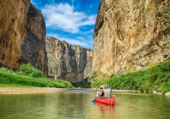 A person in a red canoe paddles through the towering limestone cliffs of Santa Elena Canyon on the Rio Grande, Big Bend National Park.