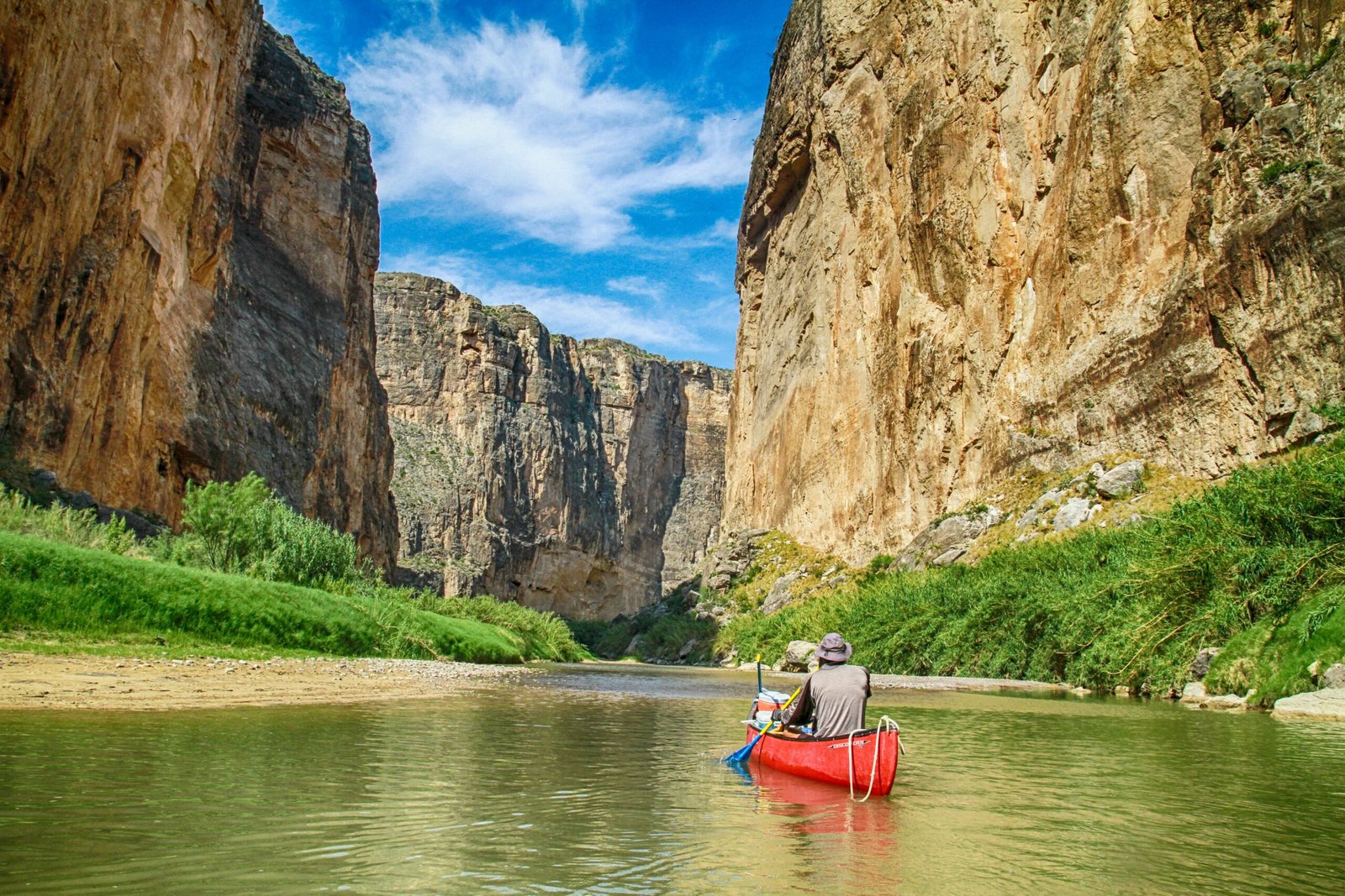 A person in a red canoe paddles through the towering limestone cliffs of Santa Elena Canyon on the Rio Grande, Big Bend National Park.