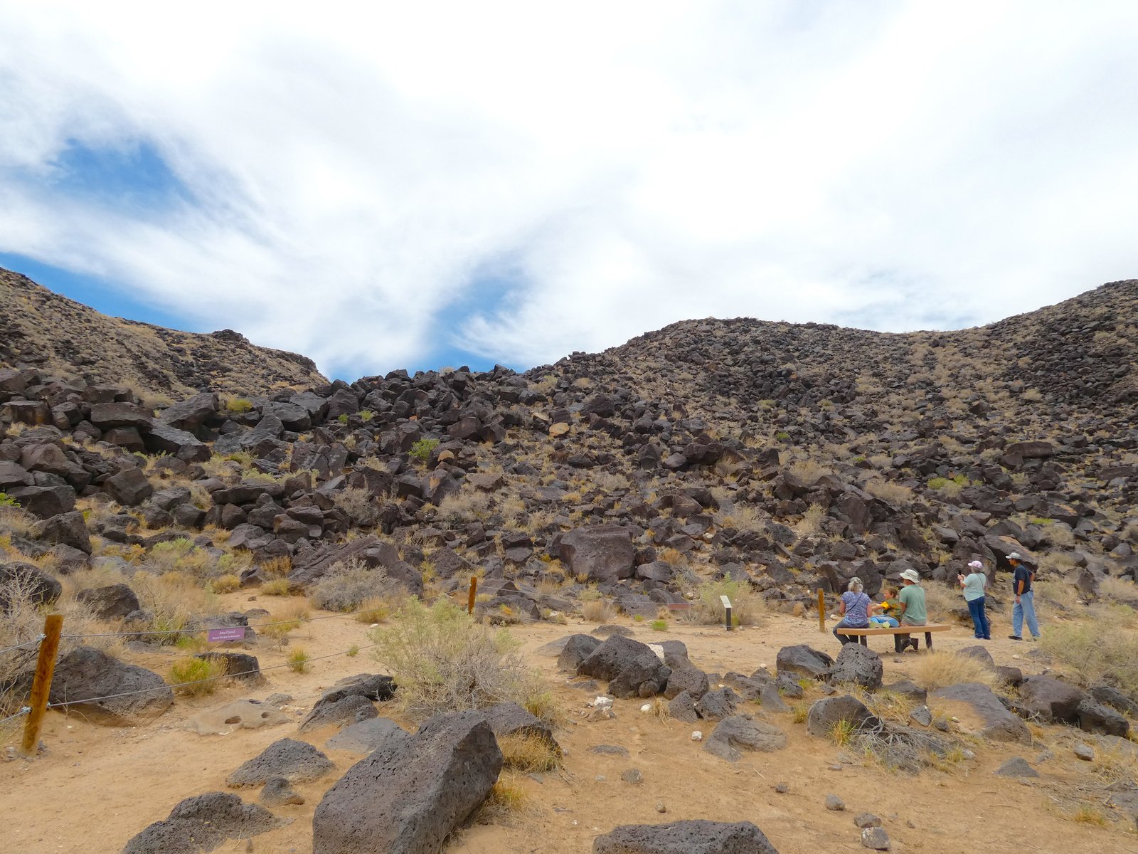 Hikers and visitors walking along the trail and viewing petroglyphs on the volcanic basalt rocks at Petroglyph National Monument.
