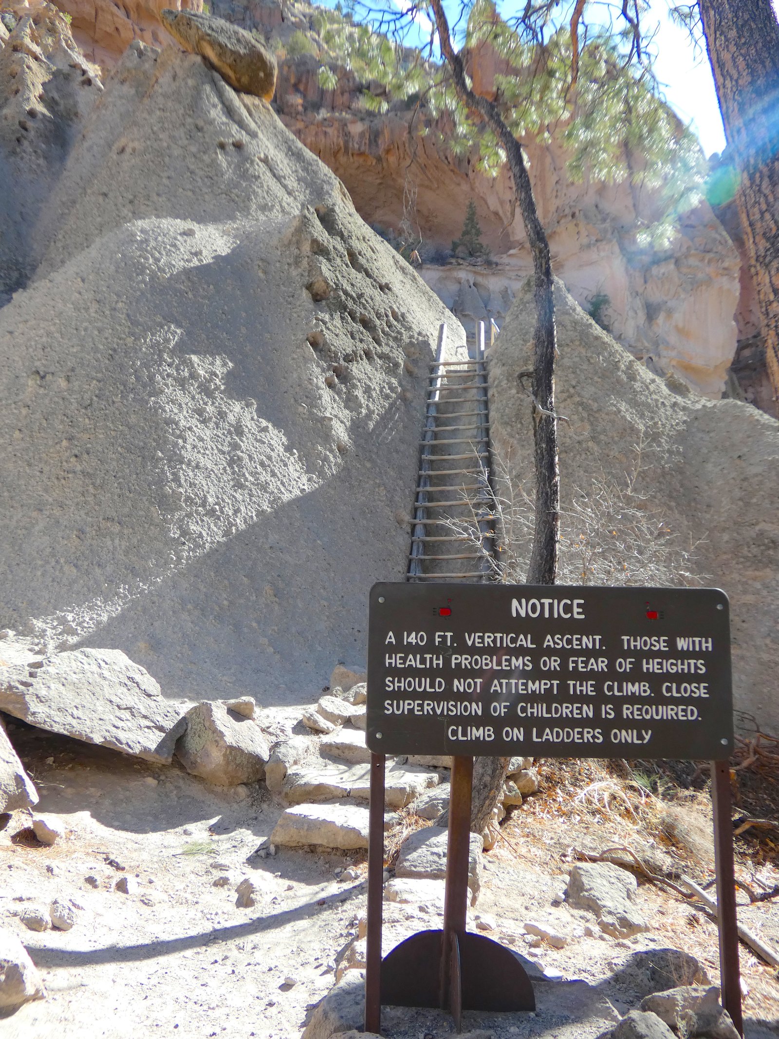 A National Park warning sign at the base of the Alcove House ladders detailing the 140-foot vertical ascent and health restrictions at Bandelier National Monument.