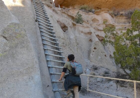 A hiker climbing the steep wooden ladder up the cliffside to Alcove House at Bandelier National Monument in New Mexico.