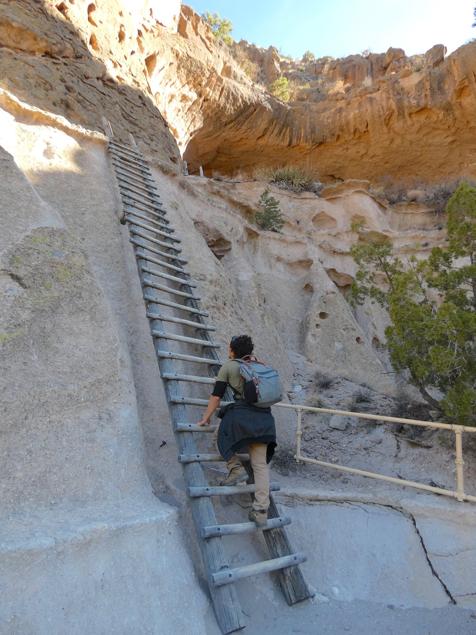 A hiker climbing the steep wooden ladder up the cliffside to Alcove House at Bandelier National Monument in New Mexico.