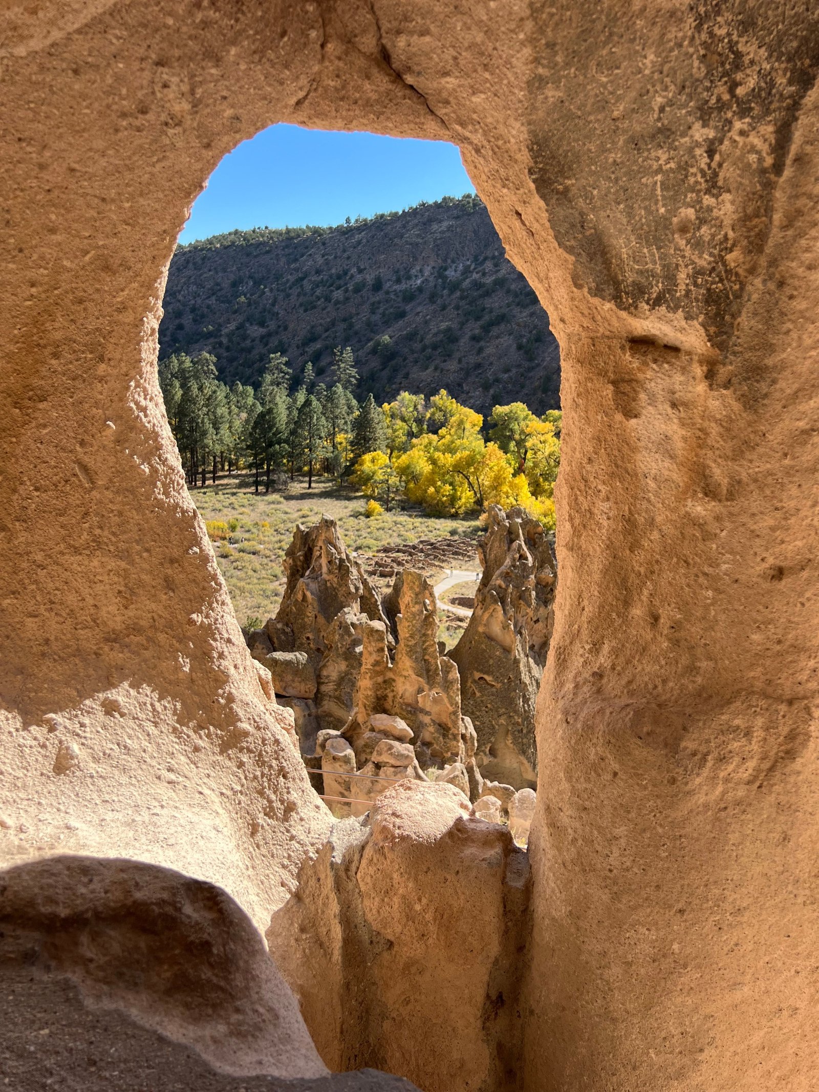 Looking out through a hand-carved cliff dwelling cavate at Bandelier National Monument, showing a view of the canyon and volcanic rock formations.