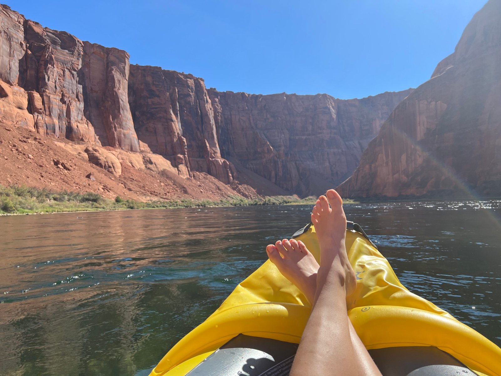 feet on kayak on the river with red canyon walls surrounding