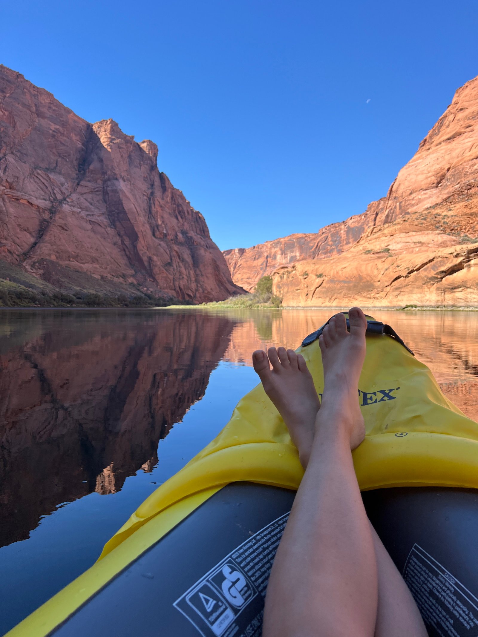 persons feet on kayak in water with canyon walls in the distance