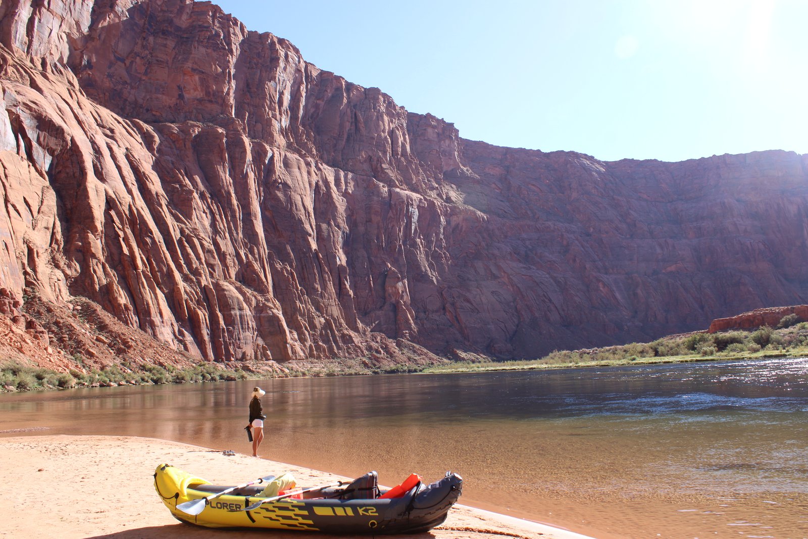 kayak on beach with person and red canyon walls in the distance