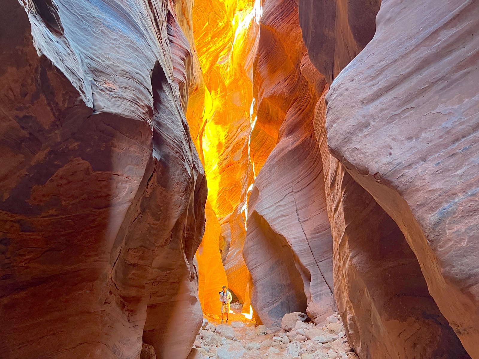 person standing in slot canyon with orange light coming from above