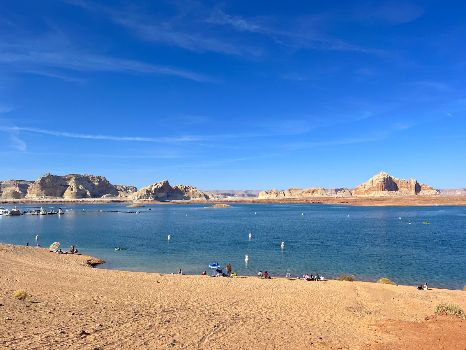 view of sandy shoreline with blue water and red rocks in the distance