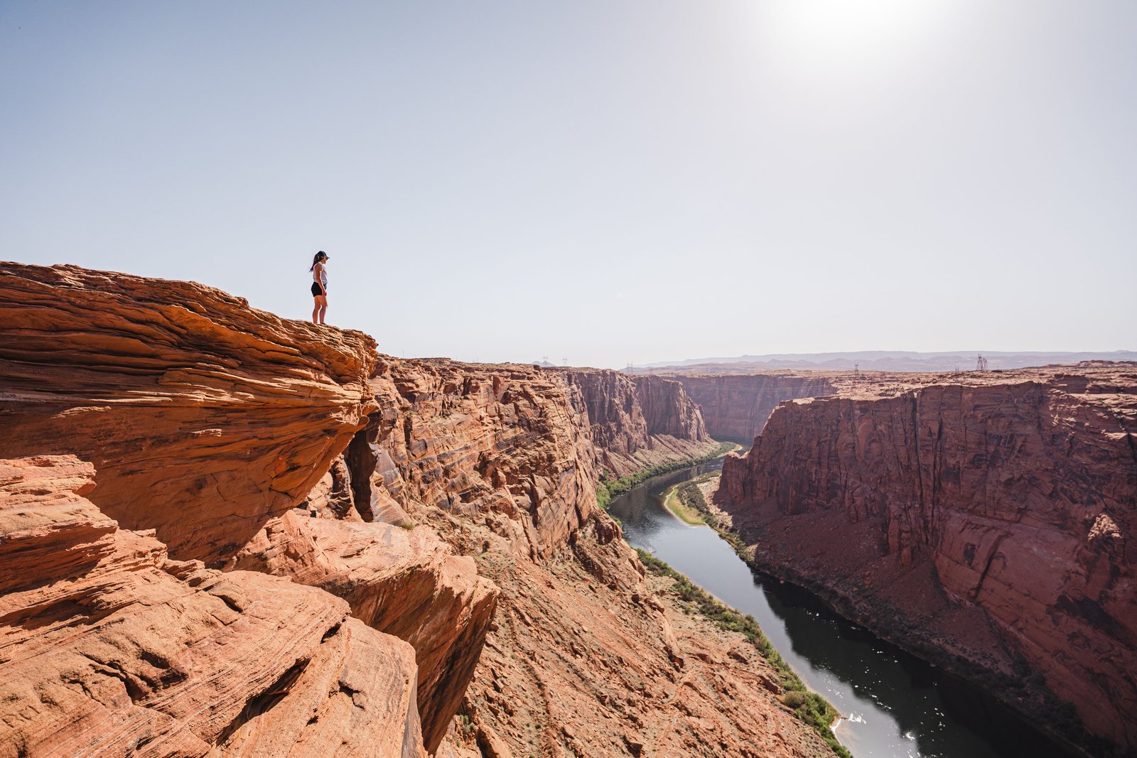 person standing on rocky cliff edge overlooking a deep canyon with a river running through it