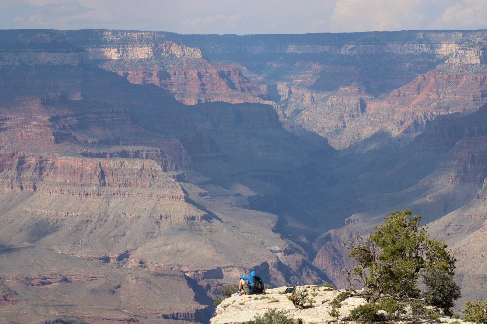 person in distance sitting on cliff edge with Grand Canyon in the background