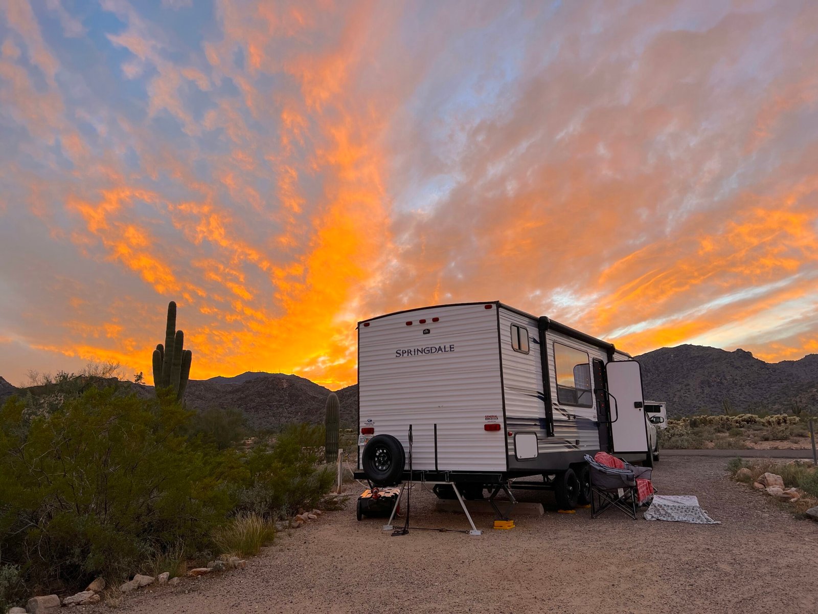 Travel trailer parked in an Arizona desert campground at sunset with saguaros and mountains.