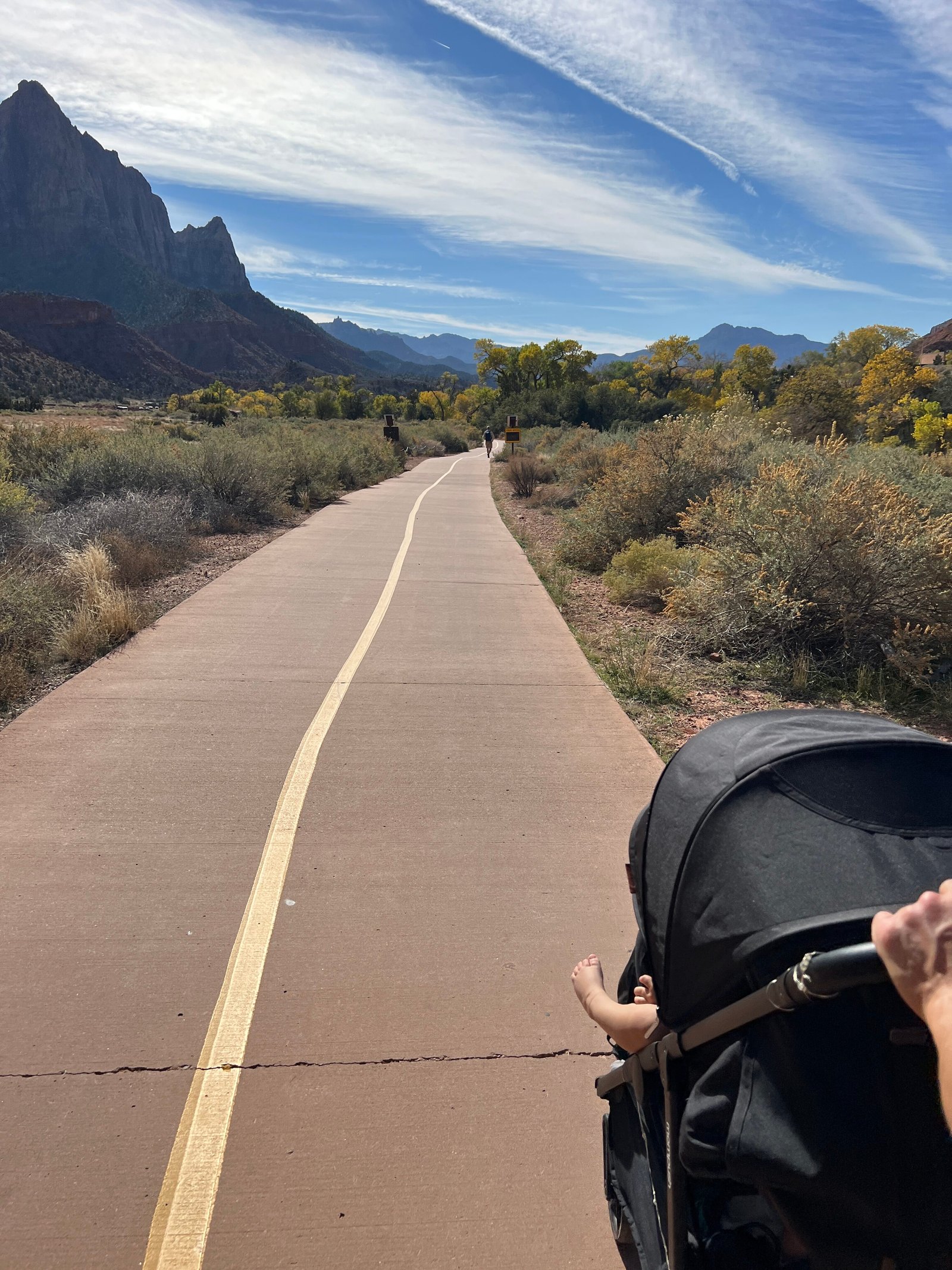First-person view of pushing a stroller along the paved path on the Pa'rus Trail in Zion National Park with canyon walls in the background.