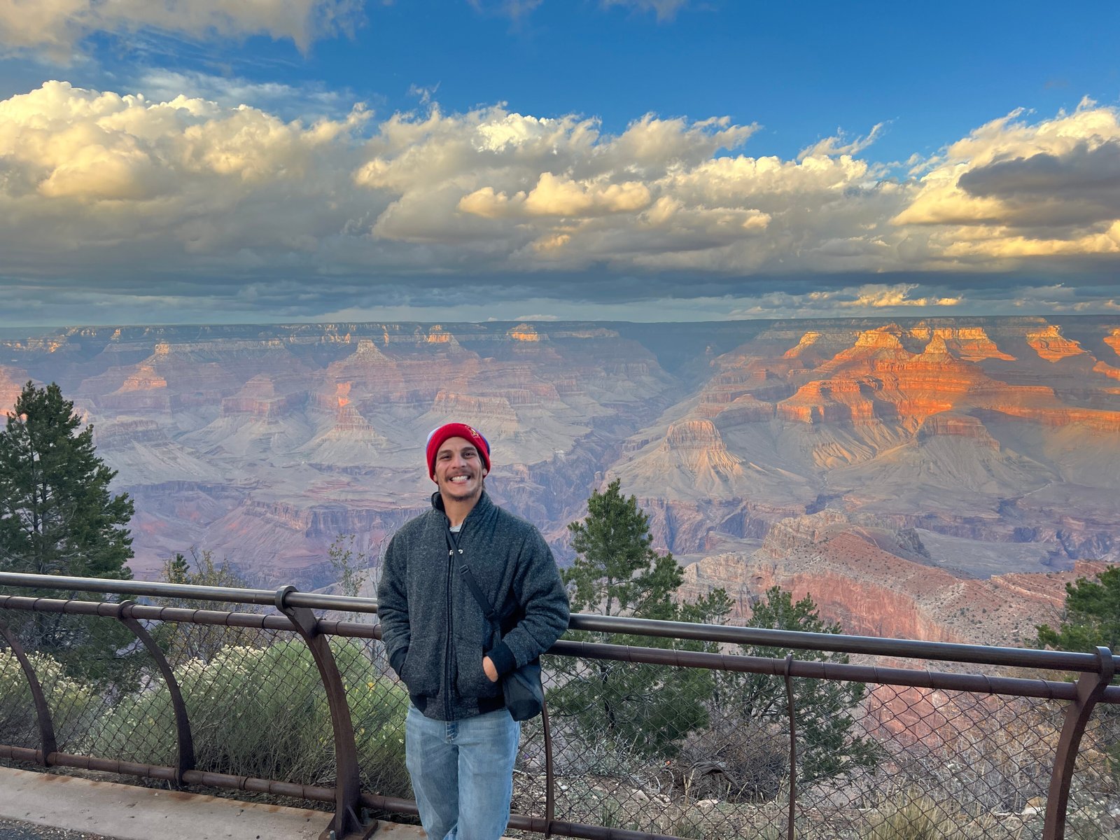 person standning smiling along railing with Grand Canyon in the distance