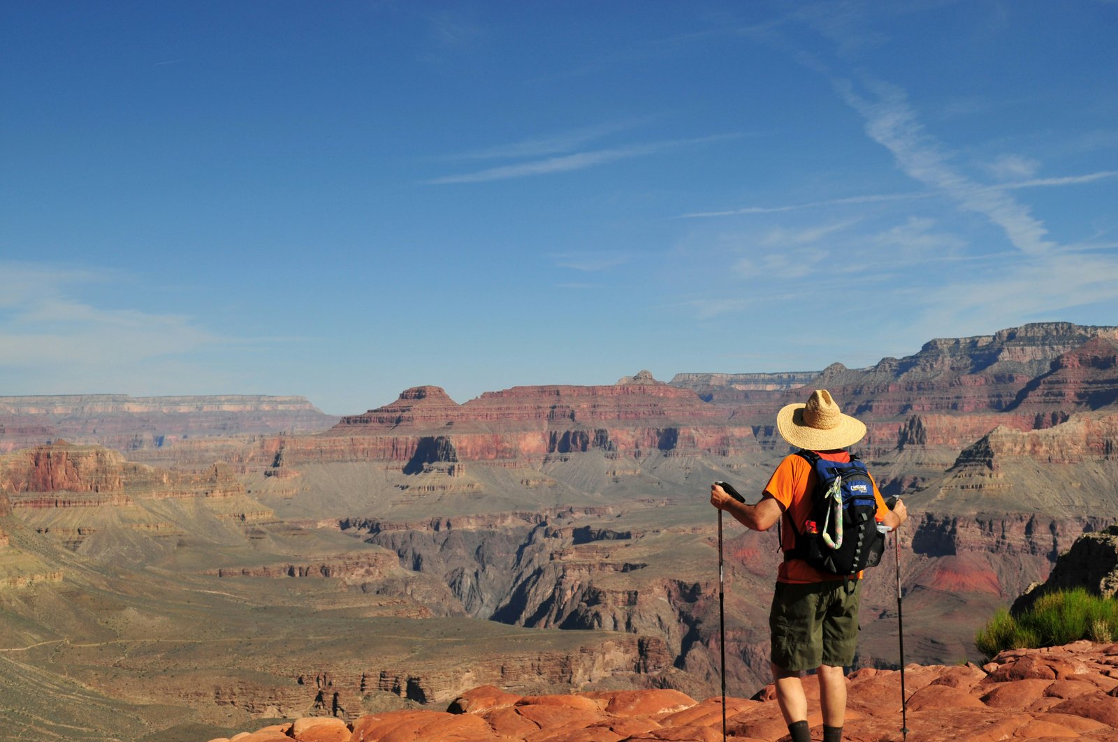 person standing with hiking sticks, hat, and backpack with Grand Canyon in the distance