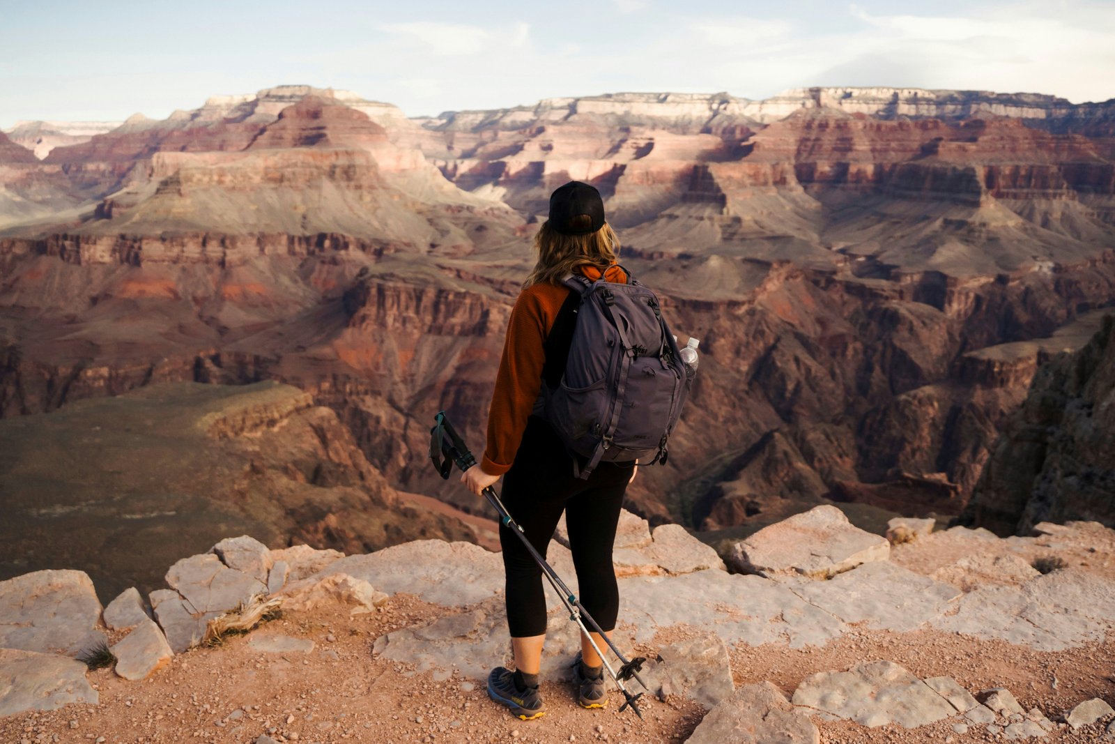 person with backpack and hiking sticks near cliff edge overlooking the Grand Canyon