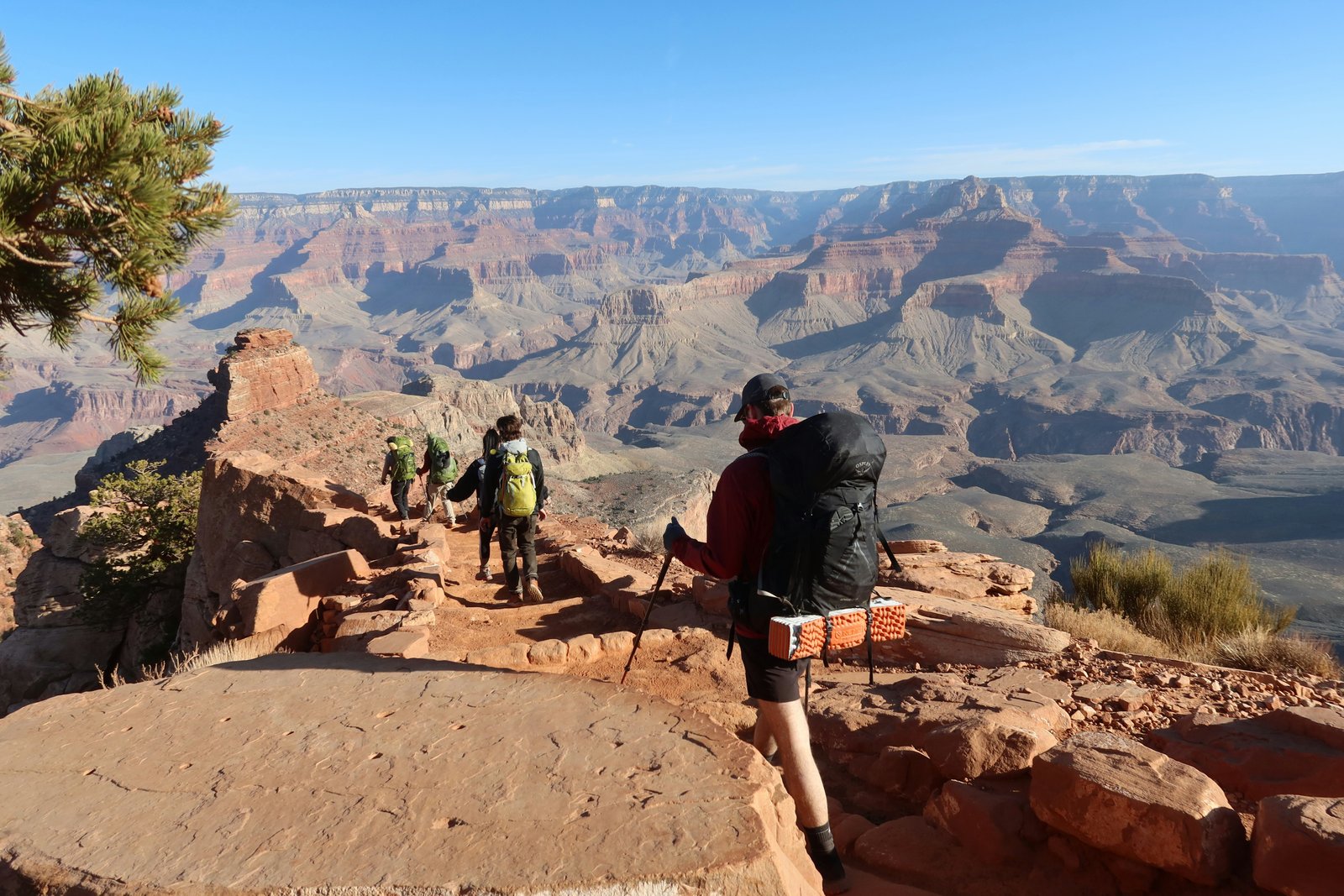 several hikers with backpacks on trail with Grand Canyon in the distance