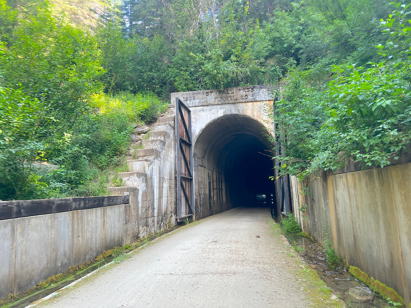 Looking directly into the dark, pitch-black concrete entrance of a rail-trail tunnel surrounded by trees on the Route of the Hiawatha.