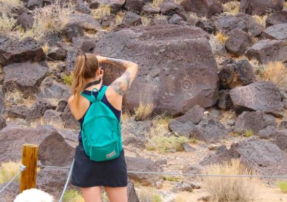 Hiker photographing ancient rock art and petroglyphs on the volcanic basalt trail at Petroglyph National Monument.