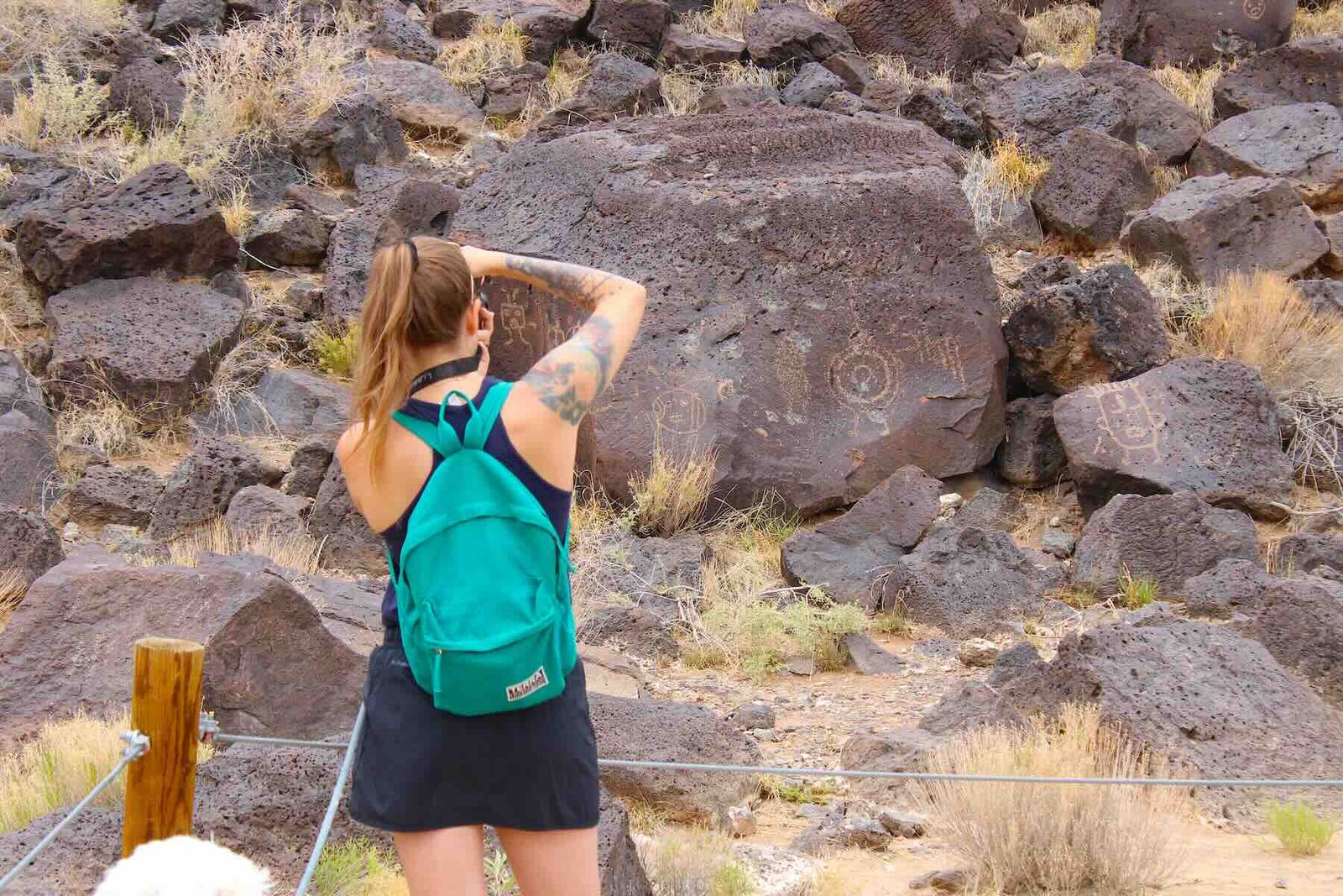 Hiker photographing ancient rock art and petroglyphs on the volcanic basalt trail at Petroglyph National Monument.